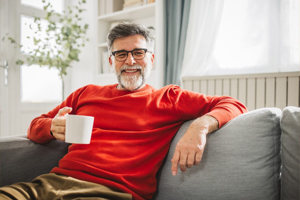 Smiling man sitting on couch with coffee mug.