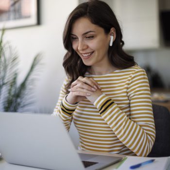 Young smiling woman with bluetooth headphones having video call at home