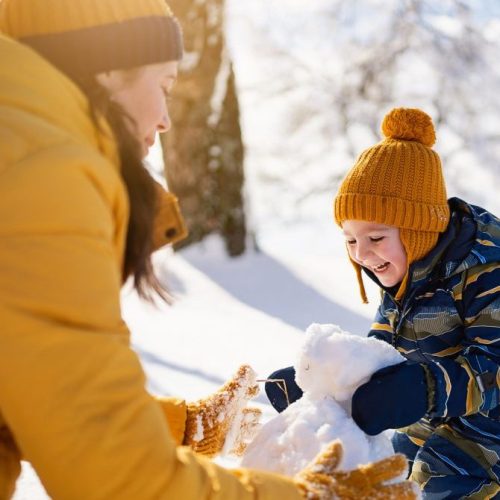 Mom and son making a snowman together.